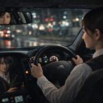 夜の街を背景に、若い女性タクシードライバーが穏やかな表情でハンドルを握り、後部座席の乗客と静かに会話しながら次の働き方について考えている様子。 A young female taxi driver drives through the city at night, calmly talking with a passenger while thinking about new career options and a more realistic way of working.